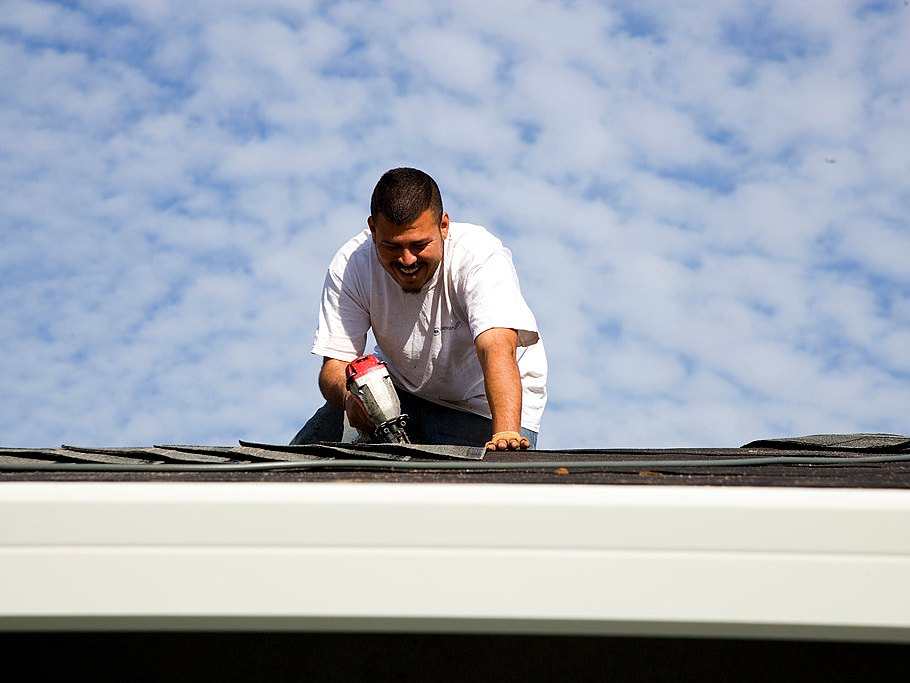 Roofer working a shingle course against a blue sky