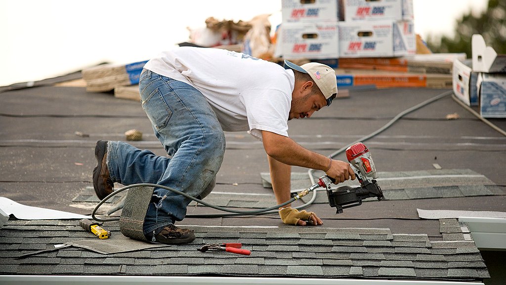 Roofer fastening architectural shingles on a residential roof